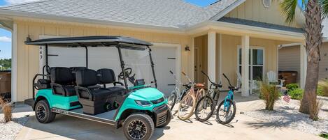 A golf cart parked in front of a house with a garage, a bicycle, and a palm tree.