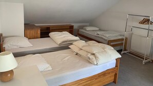 A dormitory-style room with three wooden bunk beds, a wooden desk, and a white wardrobe.