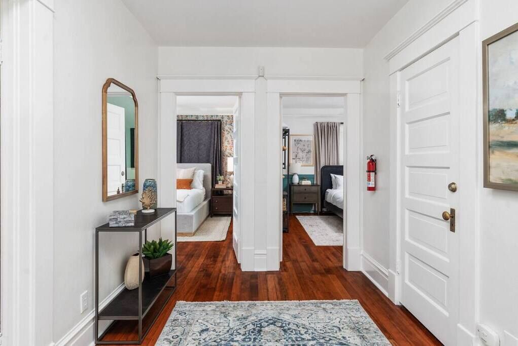 A hallway with a console table, a mirror, and a rug leading to a bedroom with a bed and nightstand.
