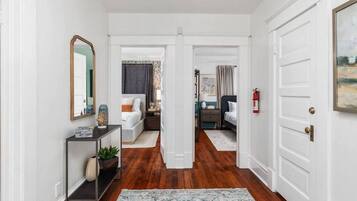 A hallway with a console table, a mirror, and a rug leading to a bedroom with a bed and nightstand.