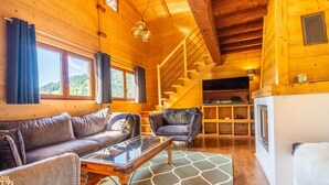 A cozy wooden cabin interior with a sofa, chairs, a glass-top coffee table, and a staircase leading to an upper level. - Cozy Chalet, 4 Bedrooms, Sleeps 9, WiFi, Near Ski Lifts, La Clusaz (La Clusaz)
