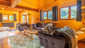 A cozy log cabin interior with a sofa set, a wooden coffee table, and a view of the forest through large windows. - Cozy Chalet, 4 Bedrooms, Sleeps 9, WiFi, Near Ski Lifts, La Clusaz (La Clusaz)