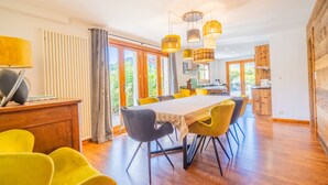 A modern dining area with a wooden table and yellow chairs, a kitchen in the background, and large windows allowing natural light. - Cozy Chalet, 4 Bedrooms, Sleeps 9, WiFi, Near Ski Lifts, La Clusaz (La Clusaz)