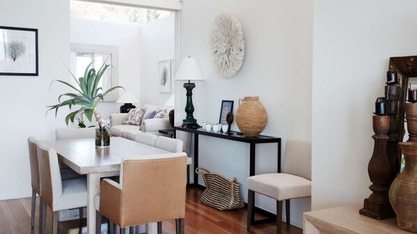 A modern living room with a dining table, sofa, and chairs. There is a large plant, a lamp, and a decorative wall piece.