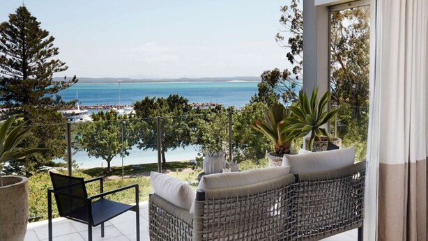 A balcony with a view of the sea, a wicker sofa, a chair, and potted plants. - The Waterview, 2 76 Magnus St -  complete style, comfort, luxury and spectacular waterviews (Nelson Bay)
