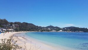 A beach with clear water, a sandy shore, and buildings in the background. - The Waterview, 2 76 Magnus St -  complete style, comfort, luxury and spectacular waterviews (Nelson Bay)