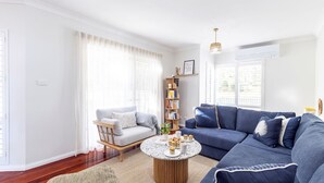 Una sala de estar con un sofá azul, una silla de madera, una mesa de centro redonda y una estantería.