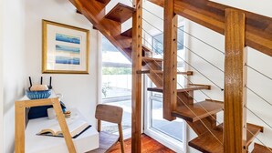 Un interior moderno con una escalera de madera, un cuadro enmarcado en la pared y una zona de estar con una mesa y una silla.