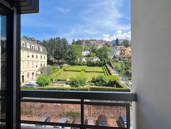 A view from a window overlooking a well-maintained garden with neatly trimmed hedges and a variety of trees.