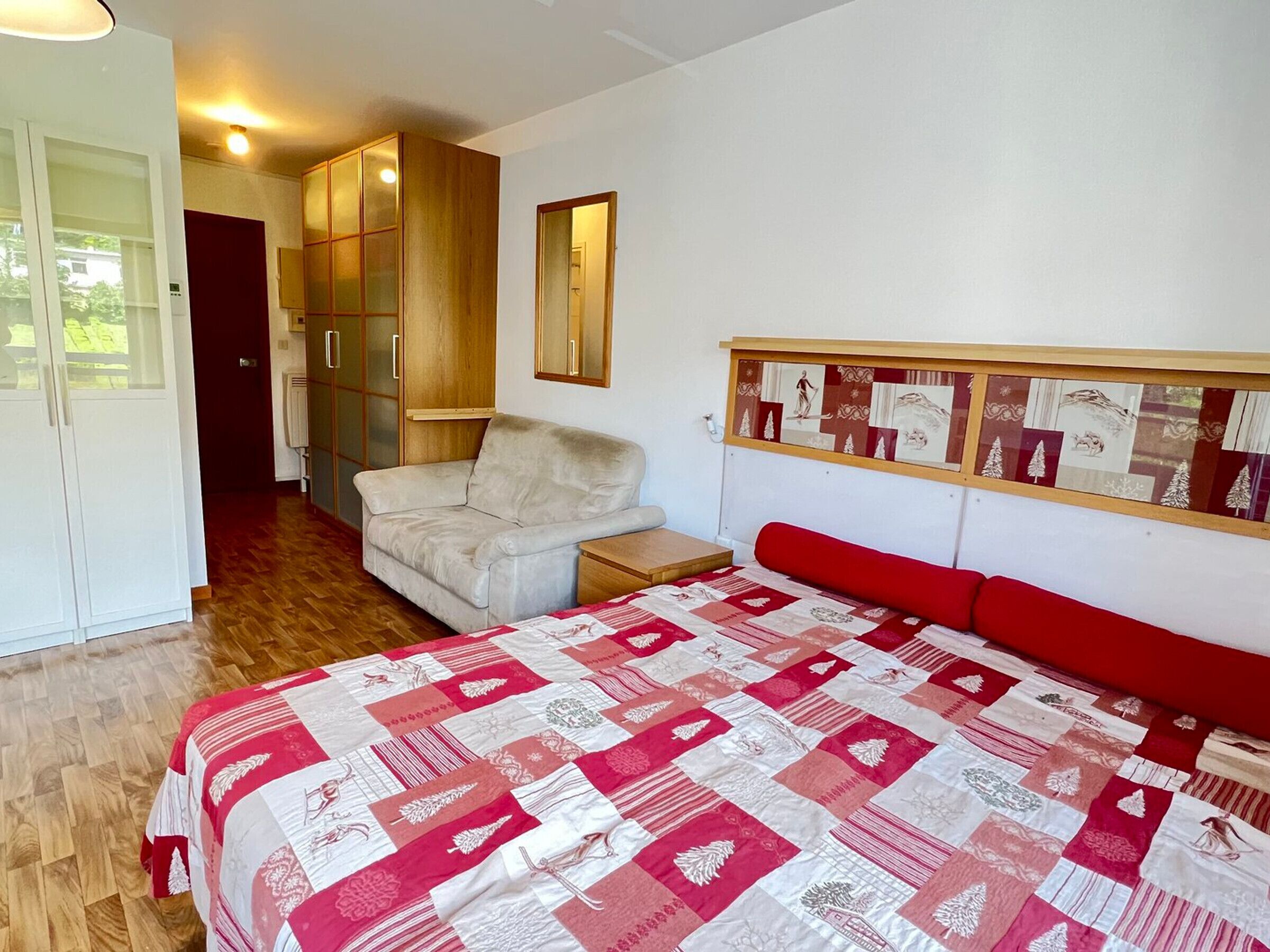 A bedroom with a bed, a chair, a wardrobe, and a mirror.