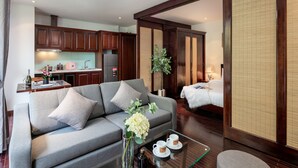 Una habitación de hotel moderna con sofá, una mesa de comedor con tazas, cama y zona de cocina.