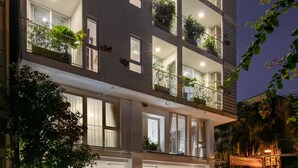 Un hotel de varios pisos con balcones, plantas en macetas y una entrada bien iluminada.
