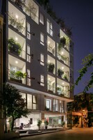 Un hotel de varios pisos con balcones, plantas en macetas y una entrada bien iluminada.