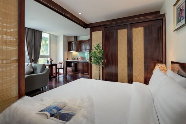 A hotel room with a large bed, a sofa, a dining area, and a kitchen in the background.