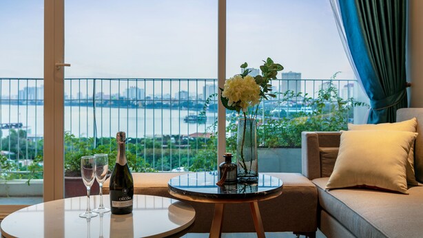 Un balcón con vistas a la ciudad y al río, una mesa con una botella de champán y copas, y un sofá con cojines.