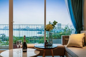 A balcony with a view of a cityscape and river, a table with a bottle of champagne and glasses, and a sofa with cushions.