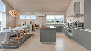Une cuisine moderne avec des murs recouverts de panneaux en bois, un îlot central et un coin repas comprenant une table et des chaises.