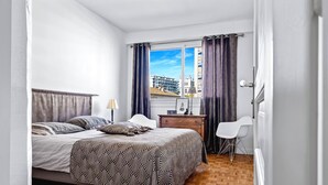 A bedroom with a bed, bedside table, lamp, chair, and a window with curtains.
