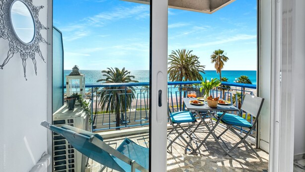 A balcony with a view of the sea, a table with chairs, and a decorative mirror.