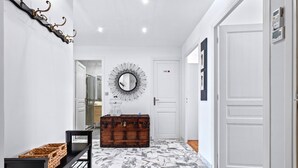 A hallway with a marble floor, a wooden chest, a black bench, and a wall-mounted mirror.