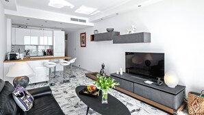 A modern living room with a sofa, coffee table, TV, and a kitchen area in the background.