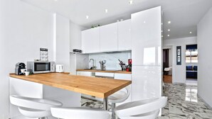 A modern kitchen with white cabinets, a wooden countertop, and white bar stools.