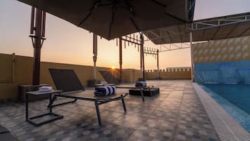 A poolside area with lounge chairs, umbrellas, and a view of the sunset.