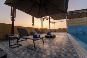 A poolside area with lounge chairs, umbrellas, and a view of the sunset. - The Royal Bihar (Danapur)