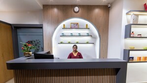 A reception desk with a woman behind it, a clock on the wall, and shelves with products in the background. - The Royal Bihar (Danapur)