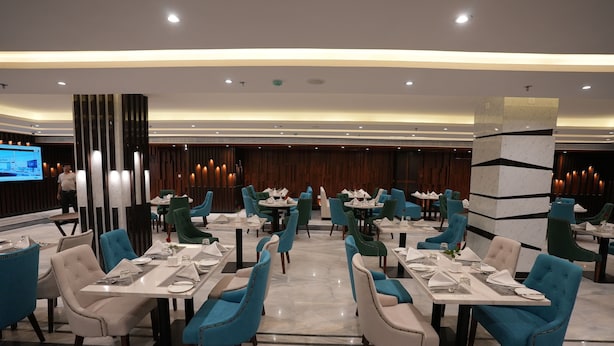 Un restaurant moderne doté de nombreuses tables et chaises, d’un grand écran diffusant du contenu et d’un mur en lambris de bois en arrière-plan.
