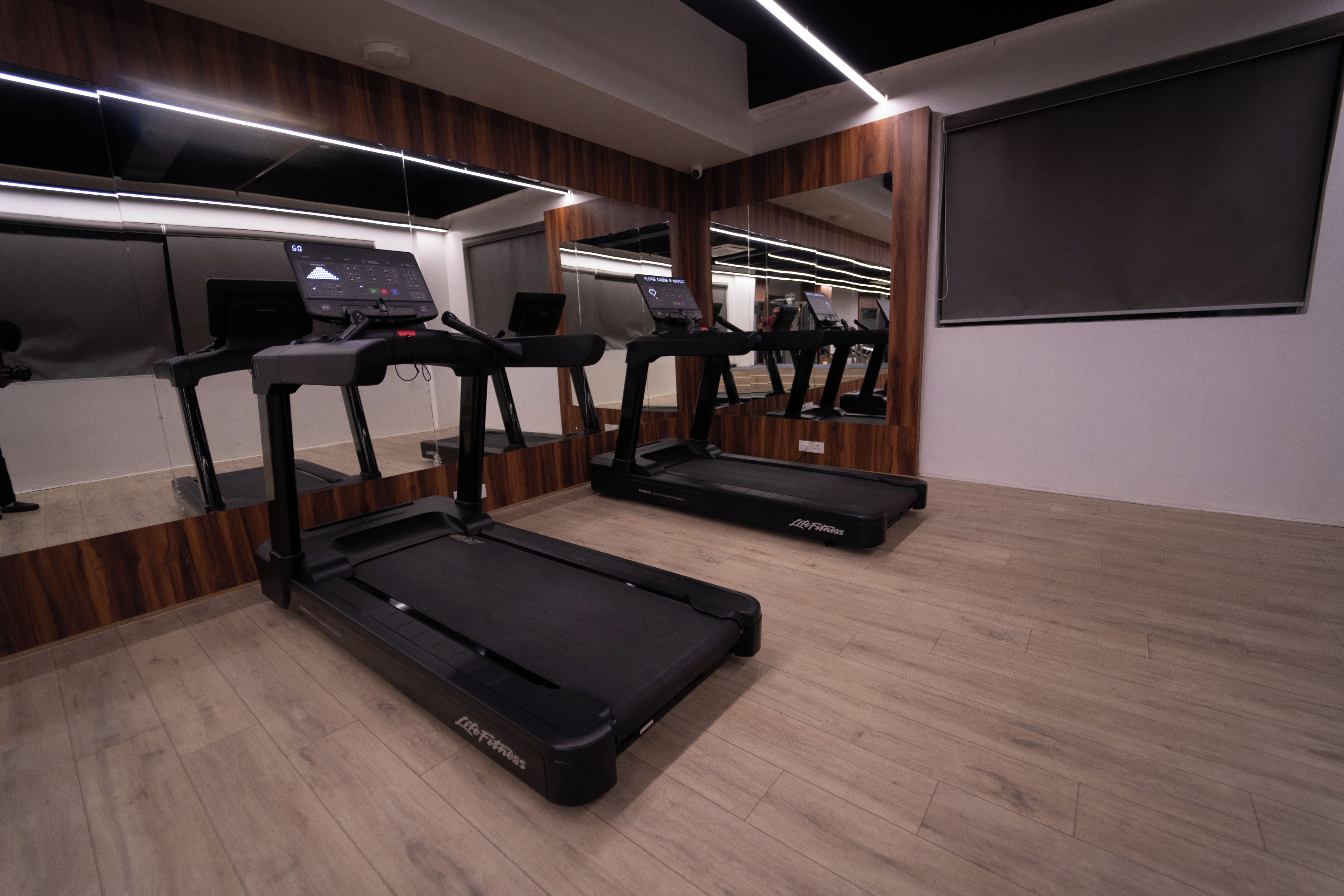 Un gimnasio con cintas de correr, suelo de madera y un espejo grande en la pared.