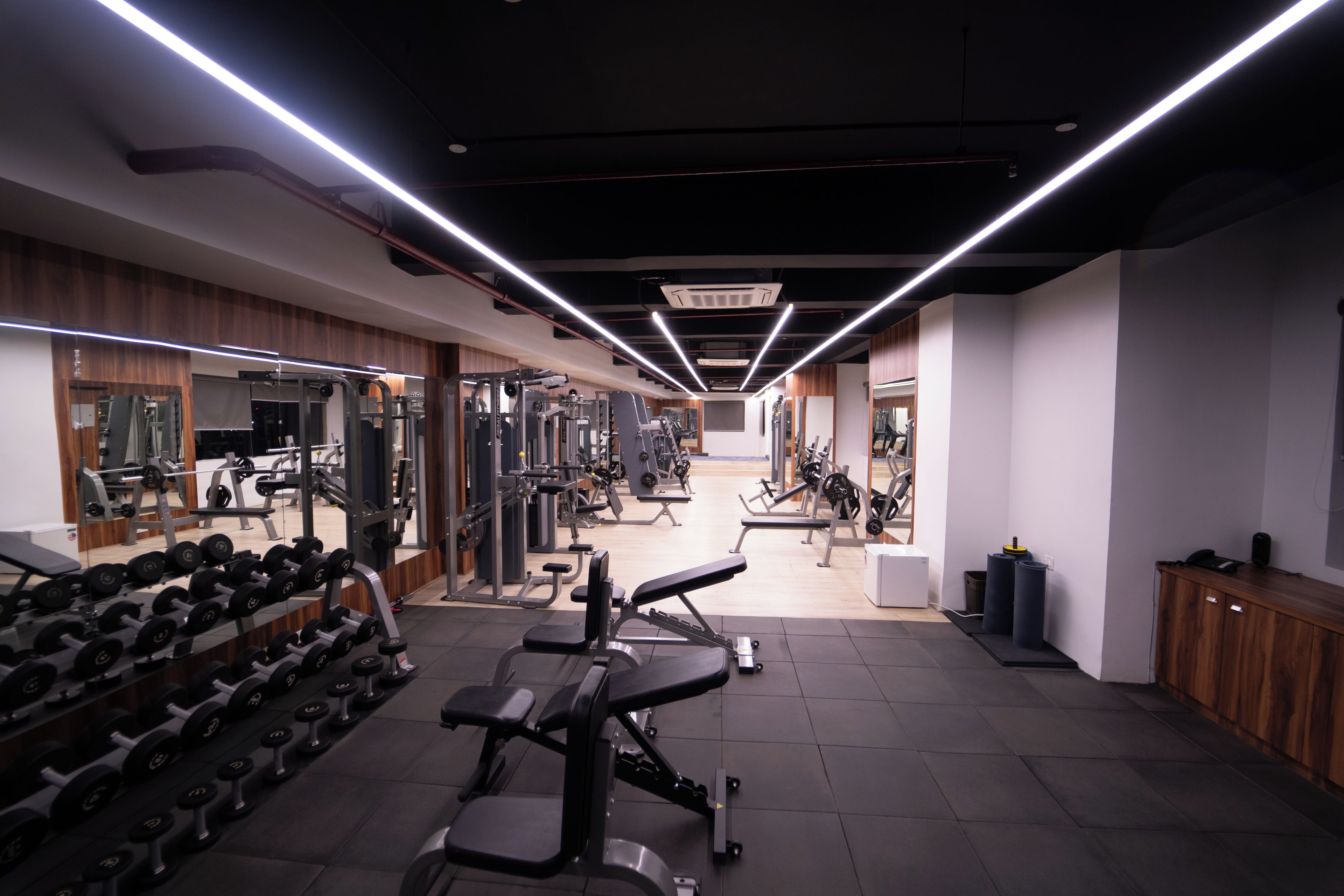 A gym with various exercise equipment, including dumbbells and weight machines, and a mirrored wall.