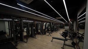 A gym with various exercise equipment, wooden flooring, and modern lighting fixtures. - The Royal Bihar (Danapur)