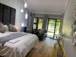 A bedroom with a large bed, a chair, a table, and a view of the outdoors.