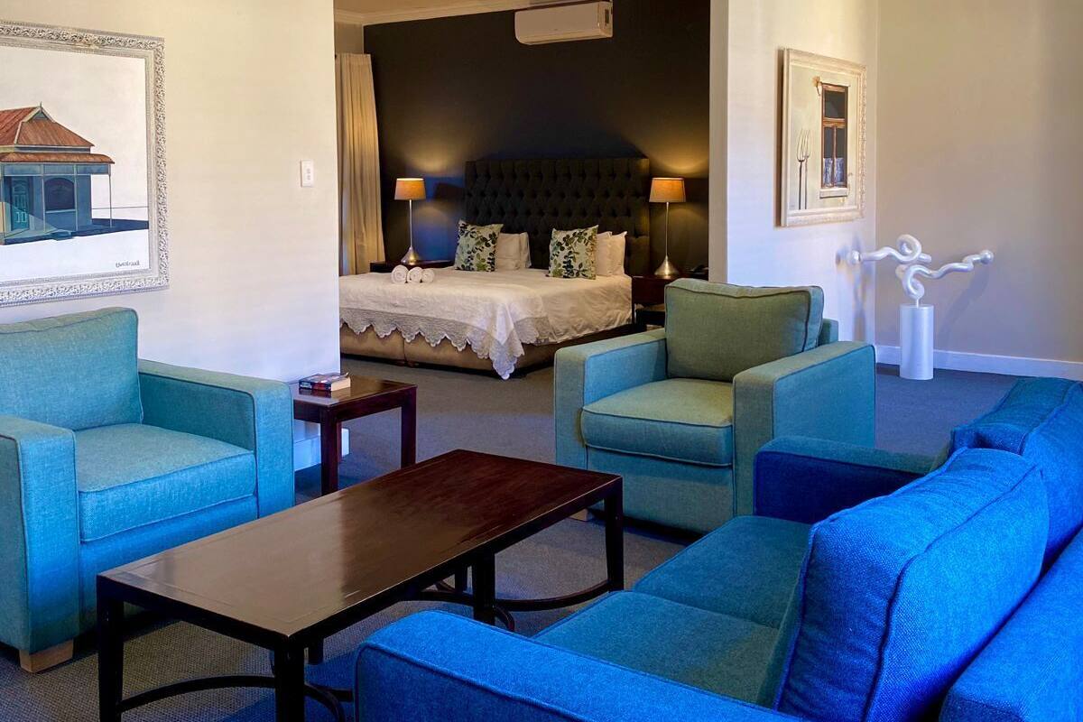 A hotel room with a large bed, two armchairs, a sofa, a small table, and a painting on the wall.