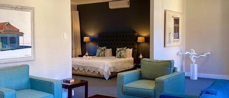 Un cuarto de hotel con una cama grande, dos sillones, un sofá, una mesita y un cuadro en la pared.