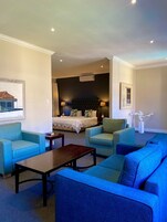 Un cuarto de hotel con una cama grande, dos sillones, un sofá, una mesita y un cuadro en la pared.