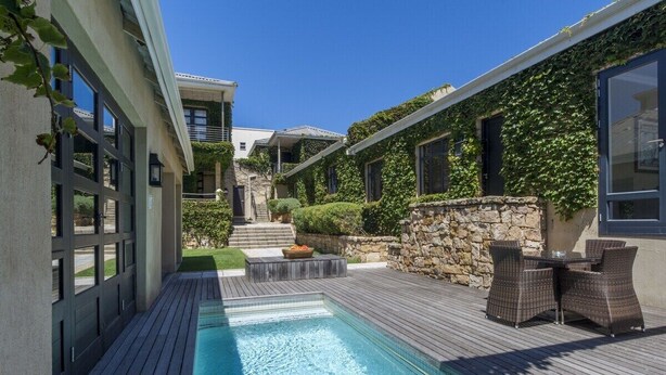 A swimming pool with a wooden deck, outdoor furniture, and a stone wall.