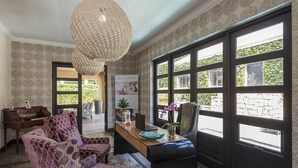 A room with patterned wallpaper, a large window with multiple panes, a wooden desk, a chair, and a hanging light fixture.