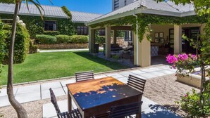 A patio with a wooden table and chairs, surrounded by a well-maintained lawn and garden.