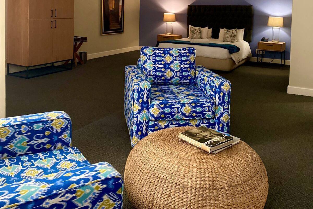 A bedroom with a bed, two bedside lamps, a large wardrobe, and a patterned armchair.