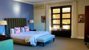 A hotel room with a bed, bedside tables, a desk, a chair, and a window with blinds.