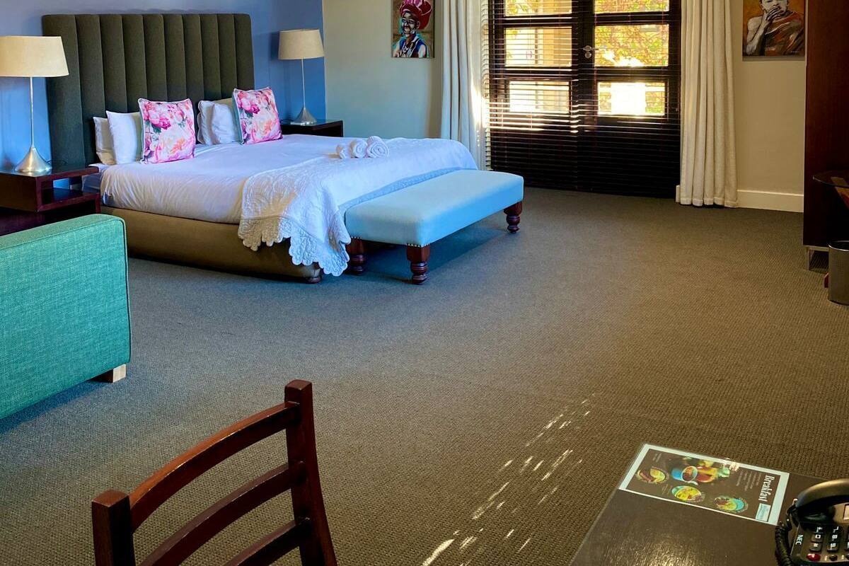 A hotel room with a bed, bedside tables, a desk, a chair, and a window with blinds.