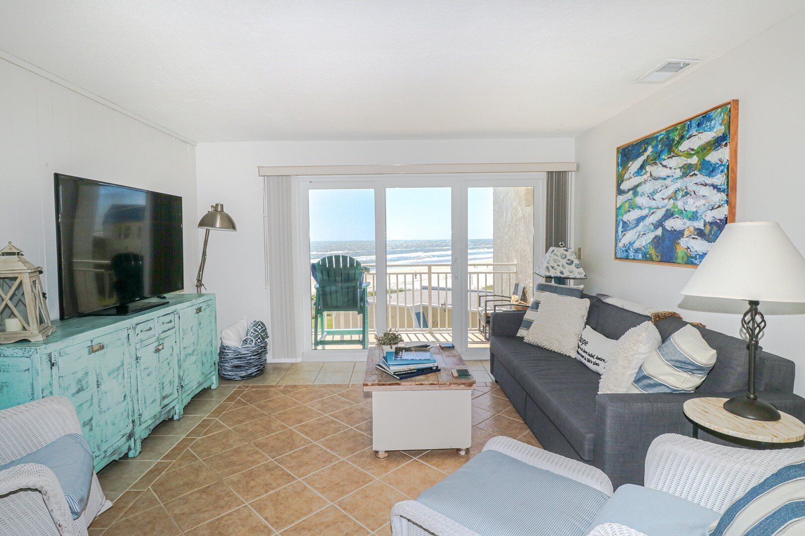 Sala de estar com televisão, sofá e varanda com vista para o mar.