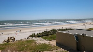 A beach view with a sandy shore, a few people, and a building in the foreground. - Tradewinds 63 - 3rd Floor Ocean View Unit with Stunning View (St. Augustine)