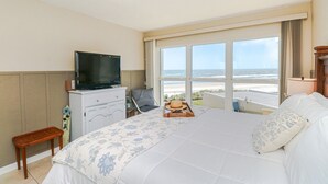 A hotel room with a bed, a television on a dresser, a small table with a tray, and a view of the beach. - Tradewinds 63 - 3rd Floor Ocean View Unit with Stunning View (St. Augustine)