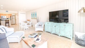A living room with a TV, a dining area, and a kitchen. - Tradewinds 63 - 3rd Floor Ocean View Unit with Stunning View (St. Augustine)