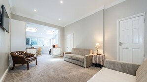 A spacious living room with a brown leather sofa, a beige sofa, and a white sofa. There is a dining area in the background with a table and chairs.