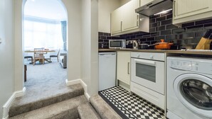 A compact kitchen with white cabinets, a microwave, a kettle, and a washing machine.