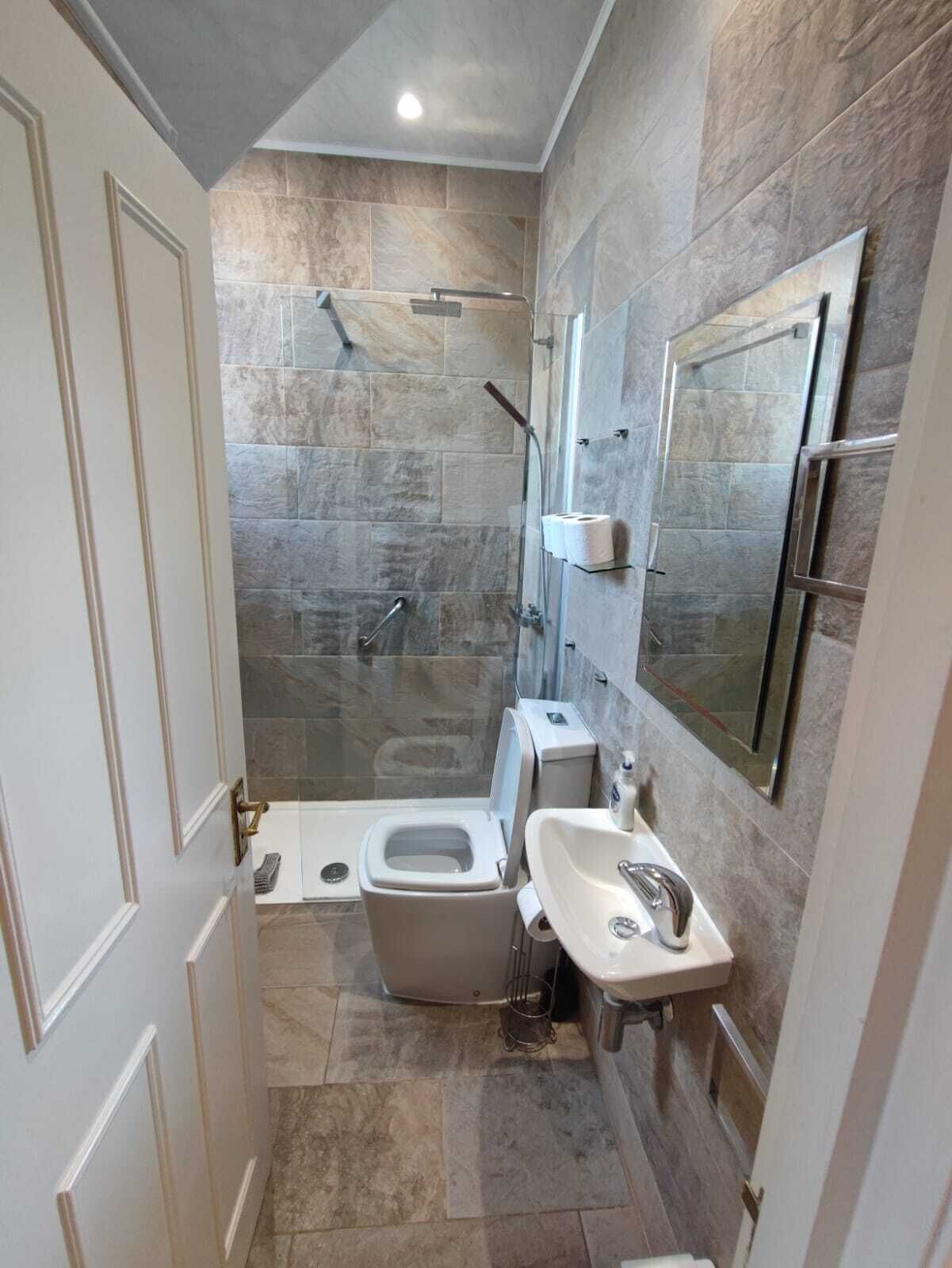 Un baño pequeño con ducha, inodoro y lavabo, con azulejos de piedra y un espejo.